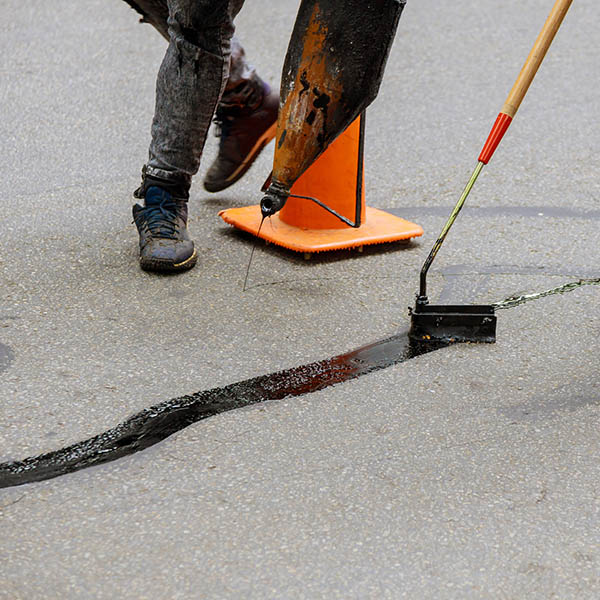 Road surface restoration work in the worker performs on road patcher work on the repair of cracks by filling and sealing with coated by bitumen emulsion asphalt surface.