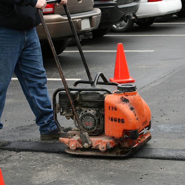 Asphalt patch repair. This image shows a tamper/vibrating machine compressing a new asphalt patch.