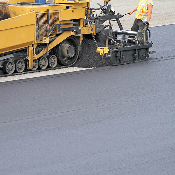 Side view of an asphalt paving machine at work paving a large parking lot, shot shallow dof and copy space.