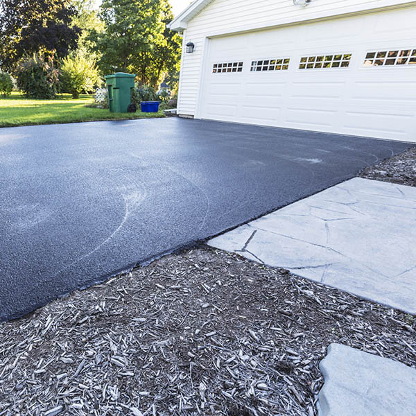 A fresh blacktop resealing job just finished on this asphalt driveway in a suburban residential district.