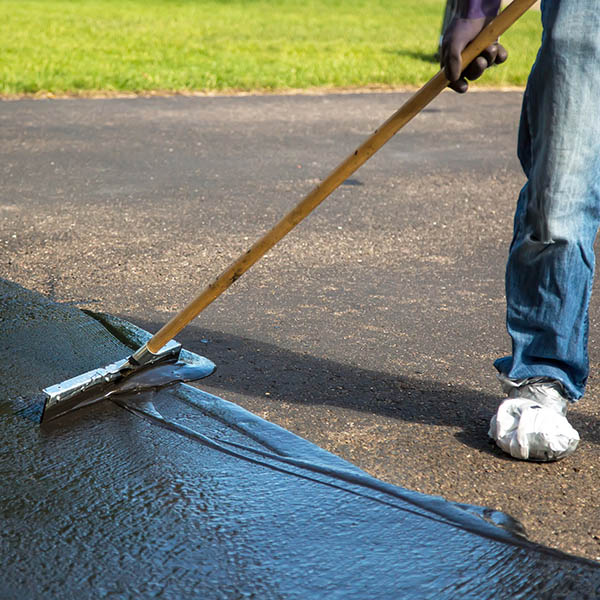 Close-up of a home owner seal coating their own driveway rather than paying someone else to do it. They are using the "broom" to spread out the sealer.