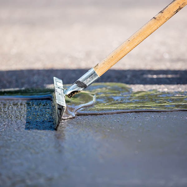Close-up of a home owner seal coating their own driveway. They are using the "broom" to spread out the sealer on the driveway. No person is visible in this particular image.