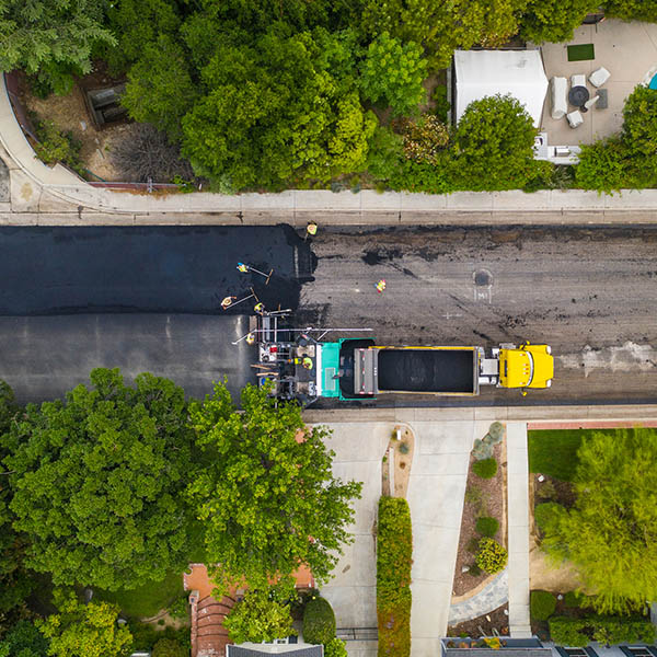Large yellow dump truck laying new asphalt on a neighborhood street in La Canada California. Construction workers use smoothing rakes to even out the surface.