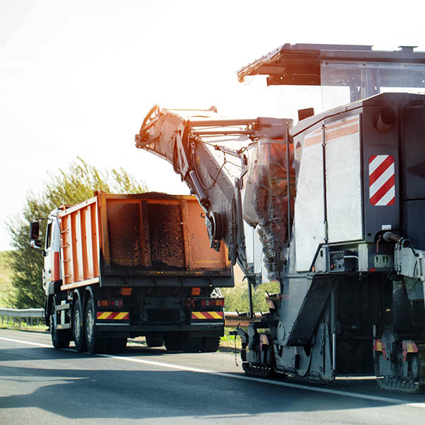 A special road-cutting machine, specifically designed for cutting asphalt layers, cuts asphalt into a dump truck with asphalt chips. Country road repair.